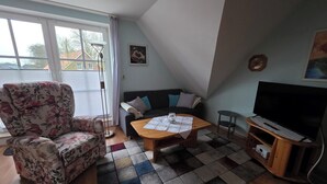 A living room with a sofa, a coffee table, a TV, and a patterned rug. - Vacation apartment Auszeit-Anker. A place for people and animals to relax. (Werdum)