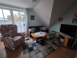 A living room with a sofa, a coffee table, a TV, and a patterned rug. - Vacation apartment Auszeit-Anker. A place for people and animals to relax. (Werdum)