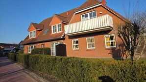 A two-story brick house with a balcony, a driveway, and a hedge. - Vacation apartment Auszeit-Anker. A place for people and animals to relax. (Werdum)