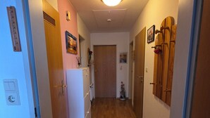 A narrow hallway with wooden flooring, a white refrigerator, and a wooden door at the end. - Vacation apartment Auszeit-Anker. A place for people and animals to relax. (Werdum)