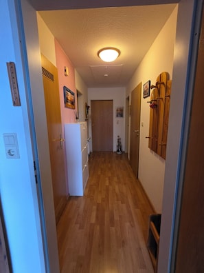 A narrow hallway with wooden flooring, a white refrigerator, and a wooden door at the end. - Vacation apartment Auszeit-Anker. A place for people and animals to relax. (Werdum)