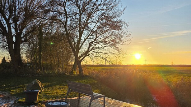 A sunset view with a bench and trash bins on a paved area. - Vacation apartment Auszeit-Anker. A place for people and animals to relax. (Werdum)