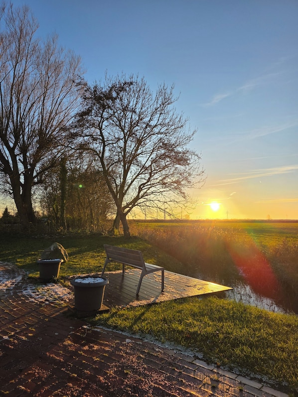 A sunset view with a bench and trash bins on a paved area. - Vacation apartment Auszeit-Anker. A place for people and animals to relax. (Werdum)