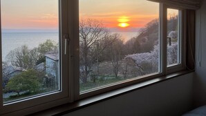 Habitació amb una finestra gran que dona a un paisatge al capvespre, amb arbres i una extensió d'aigua.