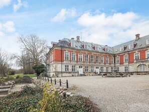 A large, historic building with a symmetrical facade, multiple windows, and a gravel courtyard.