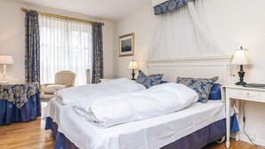 A hotel room with a large bed, a bedside table with a lamp, a chair, and a window with curtains.