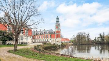 A historic building with a prominent tower, a body of water in the foreground, and a pathway leading to the building.