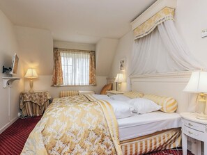 A hotel room with a bed, two bedside tables, a window with curtains, a bedside lamp, and a wall-mounted TV.