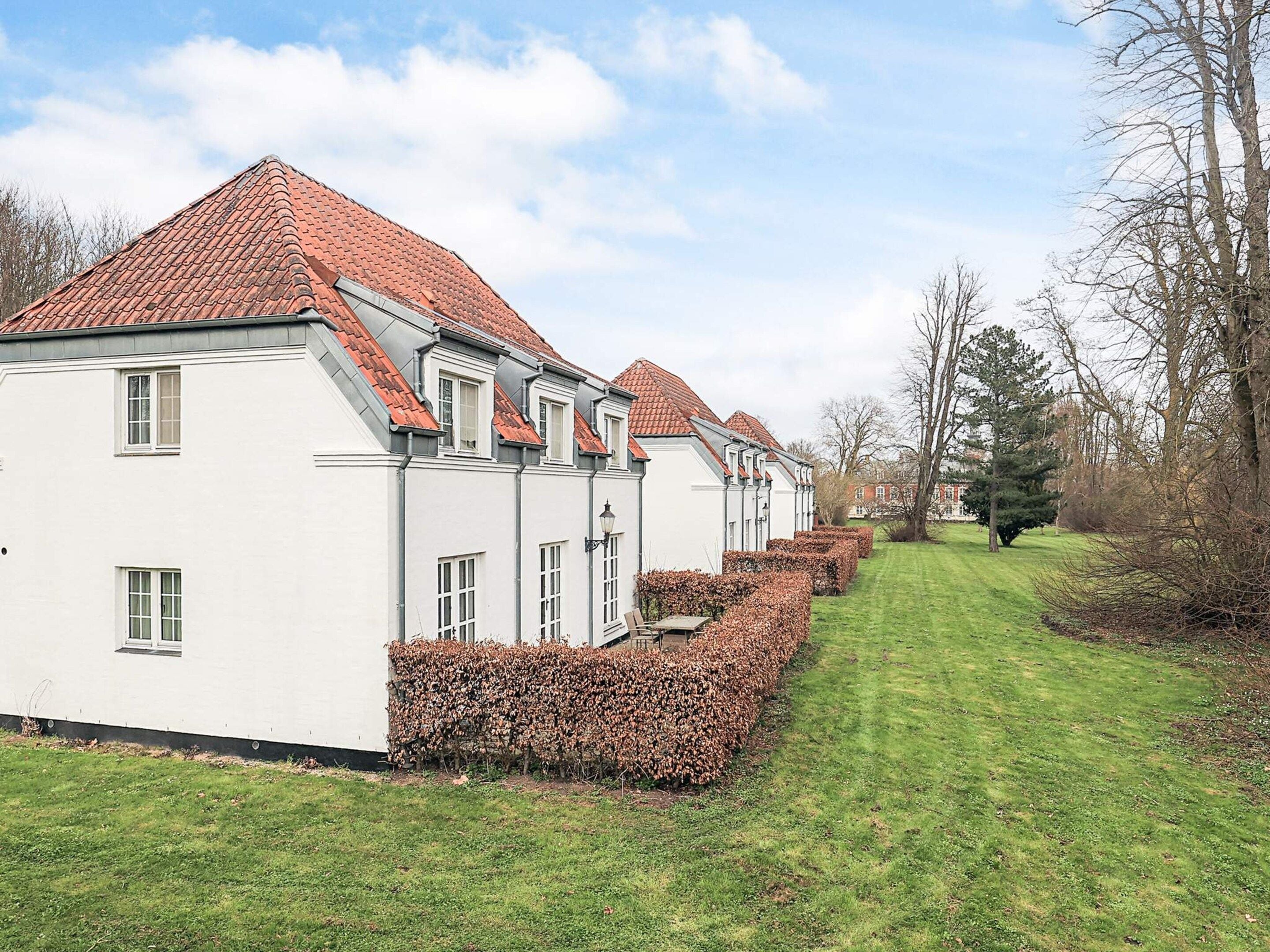 A row of white buildings with red-tiled roofs and a well-maintained lawn.