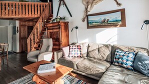 Una sala de estar con un sofá de cuero, una mesa de centro de madera, una escalera y un trozo de piel de animal colgado en la pared.