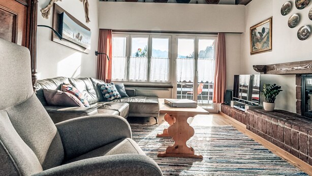 Una sala de estar con sofá, mesa de centro de madera, chimenea y vistas amplias a través de grandes ventanales.
