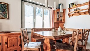 Una mesa de comedor de madera con sillas, un armario y lámparas colgantes en una habitación con ventanas amplias.