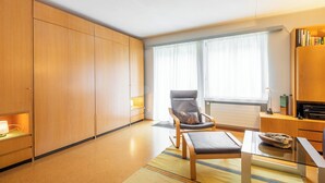 Quarto de hotel moderno com um guarda-roupa espaçoso, uma poltrona confortável, uma mesa de centro de vidro e vista para o exterior através de amplas janelas.