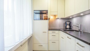 Uma cozinha compacta com janela, forno embutido, cafeteira e pia.