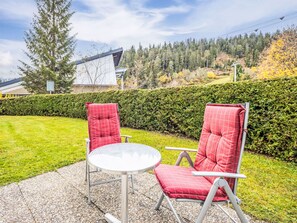 An outdoor seating area with two red chairs and a round table, surrounded by a hedge and a grassy lawn. - Val Signina 7-1 by Interhome (Laax)