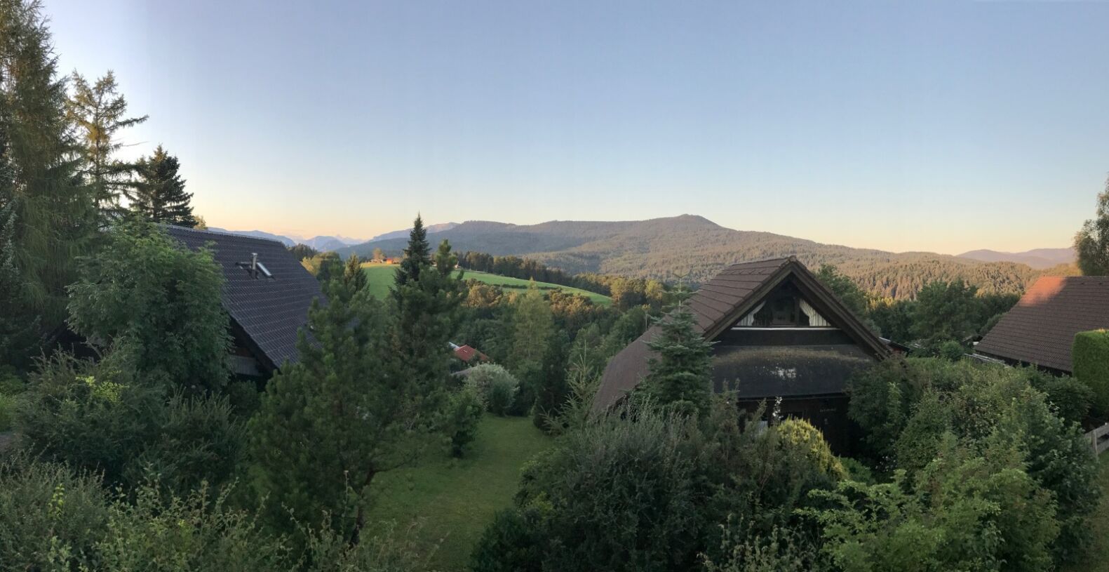A residential area with houses surrounded by dense greenery and a mountain range in the background.