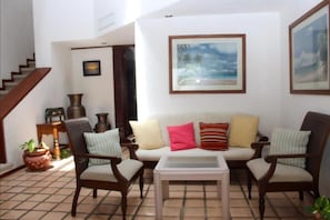 Ein Wohnzimmer mit einer Couch, zwei Sesseln, einem Couchtisch und einer Treppe.