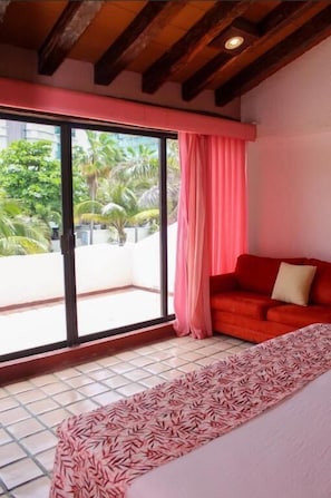 Ein Zimmer mit einem roten Sofa, einem gemusterten Teppich, einer Schiebeglastür zum Balkon und einer Decke mit freiliegenden Holzbalken.