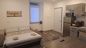 A compact room with a bed, a small table, a kitchenette, and a window with blinds. - B&B La Palma - Free Private Parking (Cuasso al Piano)