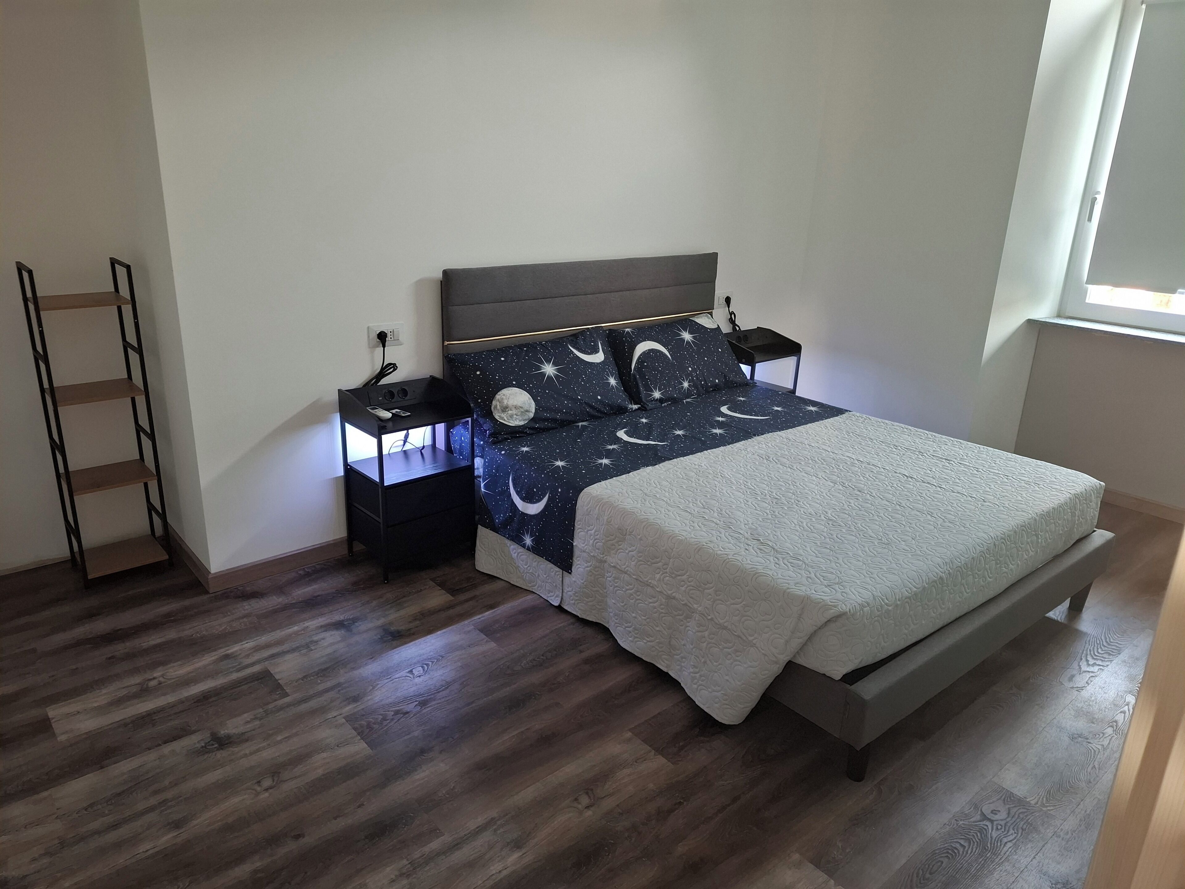 A bedroom with a bed, nightstands, a ladder, and a window.