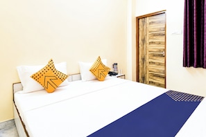 Une chambre d’hôtel avec un lit, des oreillers, une porte en bois et un rideau.