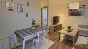 A living room with a dining table, chairs, a TV, a sofa, a coffee table, and artwork on the walls. - 10 Mins to Takism - Central & New Modern Flat (Beyoğlu)