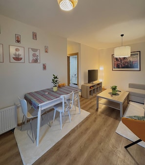 Een woonkamer met een eettafel, stoelen, een televisie, een bank, een salontafel en kunstwerken aan de muren.