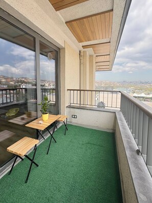 Een balkon met een vloer van groen kunstgras, een houten tafel en een plant in een pot.