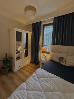 Een slaapkamer met een bed, een kledingkast, een nachtkastje, een lamp en een raam met gordijnen.