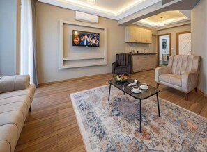 Ein modernes Wohnzimmer mit einer Couch, einem Couchtisch, einem an der Wand befestigten Fernseher und einer Küche im Hintergrund.