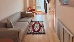 A hallway with a sofa, a chair, a patterned rug, and a door leading to a balcony with a city view. - Taksim Square-1BR Rooftop Suite 07 (Beyoğlu)