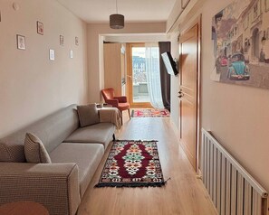 Ein Flur mit einer Couch, einem Sessel, einem gemusterten Teppich und einer Tür zu einem Balkon mit Blick auf die Stadt.