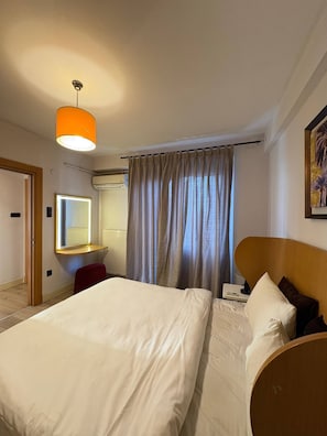 Ein Hotelzimmer mit Bett, Schreibtisch mit Stuhl, Spiegel, Klimaanlage und einem Fenster mit Vorhängen.