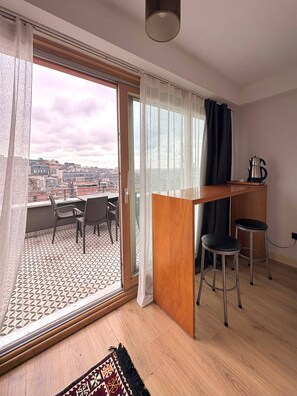 Eine moderne Wohnung mit einem Balkon, einem Holztisch, zwei Barhocker und einem gemusterten Teppich.
