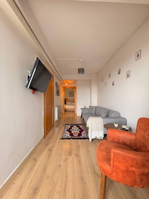 Ein Flur, der in einen Wohnbereich mit einer Couch, einem an der Wand befestigten Fernseher und einem Teppich mit Muster führt.