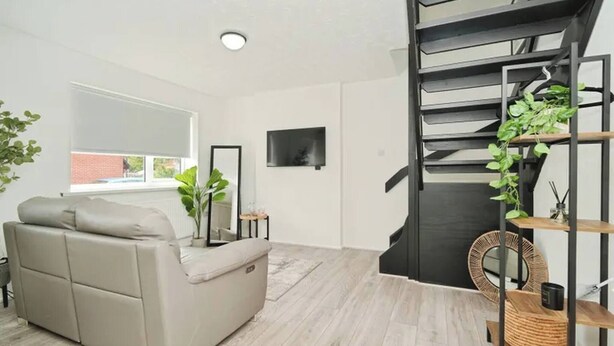 Un salon moderne avec un canapé, un téléviseur, un escalier et une plante.
