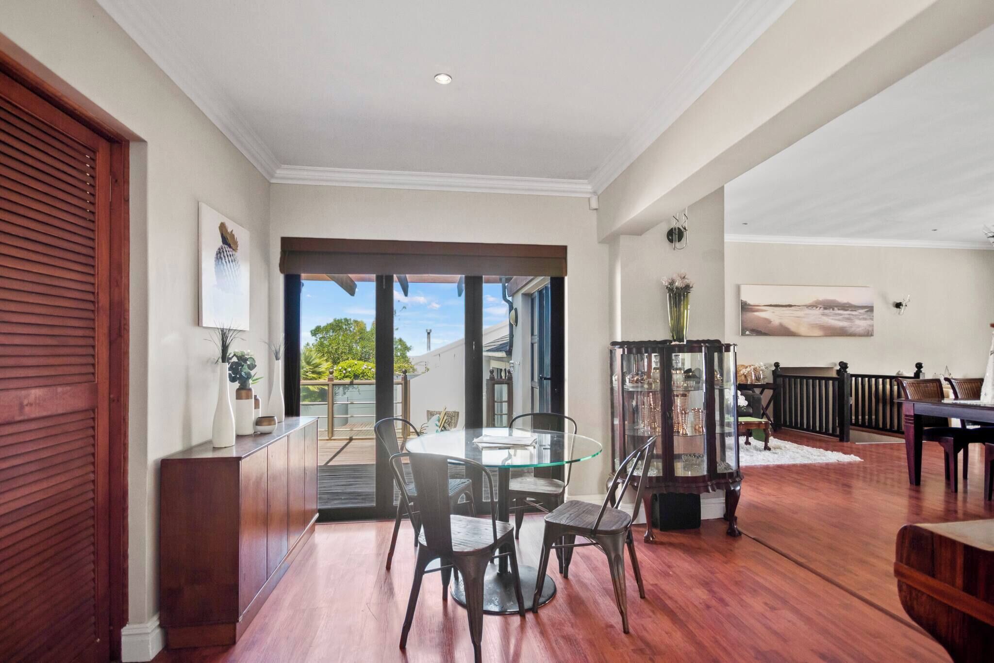 A dining area with a glass table and chairs, a wooden cabinet, and a view through a glass door to the outside.