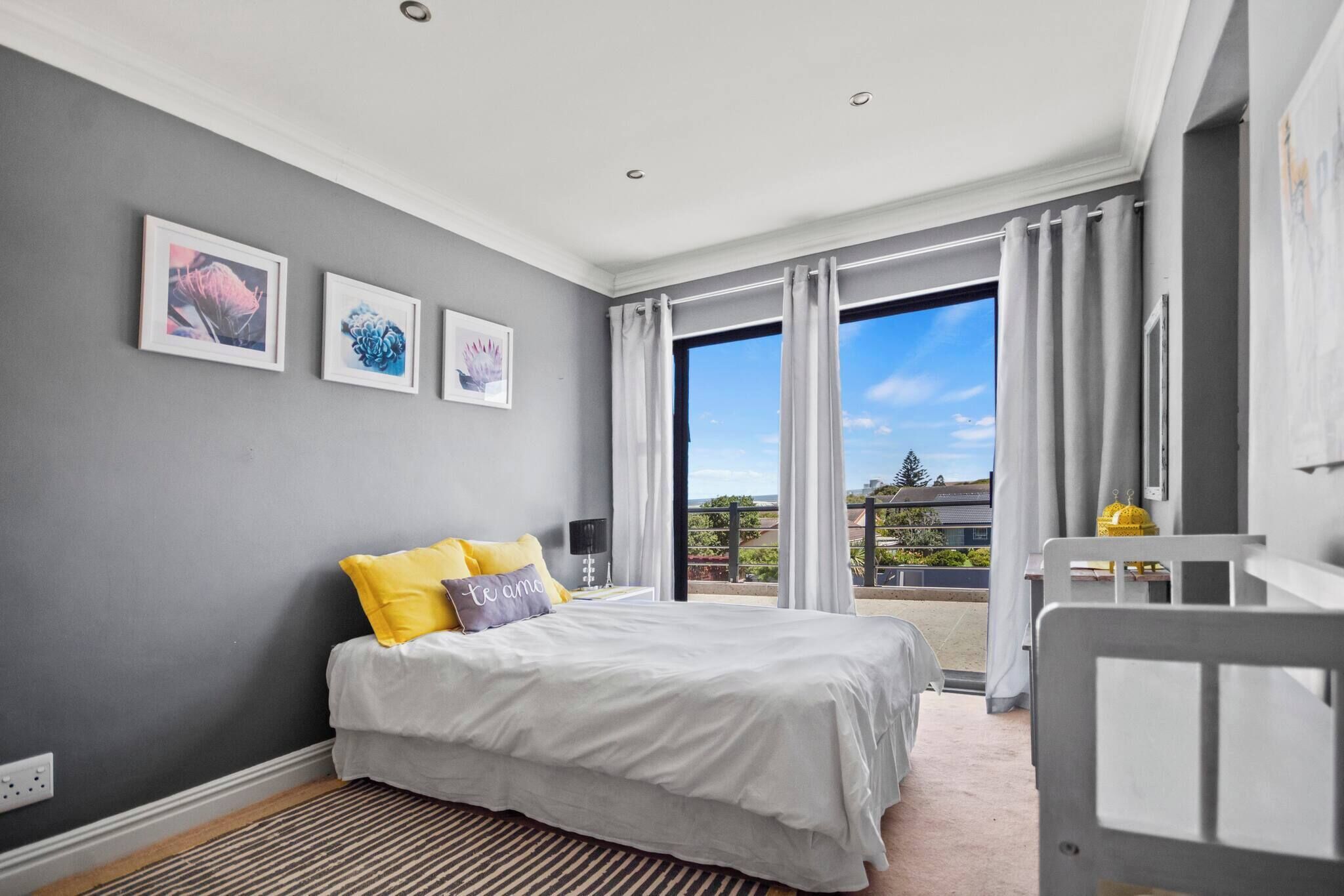 A bedroom with a bed, a nightstand, a window with curtains, and a view of the outdoors.