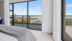 Une chambre dotée d’un grand lit et d’une porte-fenêtre coulissante donnant sur un balcon avec vue sur la plage et l’océan.