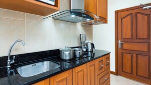Een keuken met een zwart aanrecht, een roestvrijstalen spoelbak, houten kastjes, een magnetron, een afzuigkap en een houten deur.