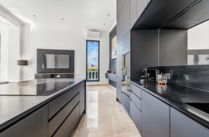A modern kitchen with dark cabinetry, a large island, and a view to the outdoors. - Magnificent 7 bedroom villa 10 minutes walk from Martinez (Cannes)