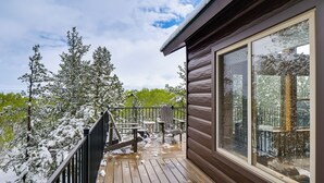Eine Holzterrasse mit schneebedeckten Bäumen, einer Glastür und einem Stuhl.