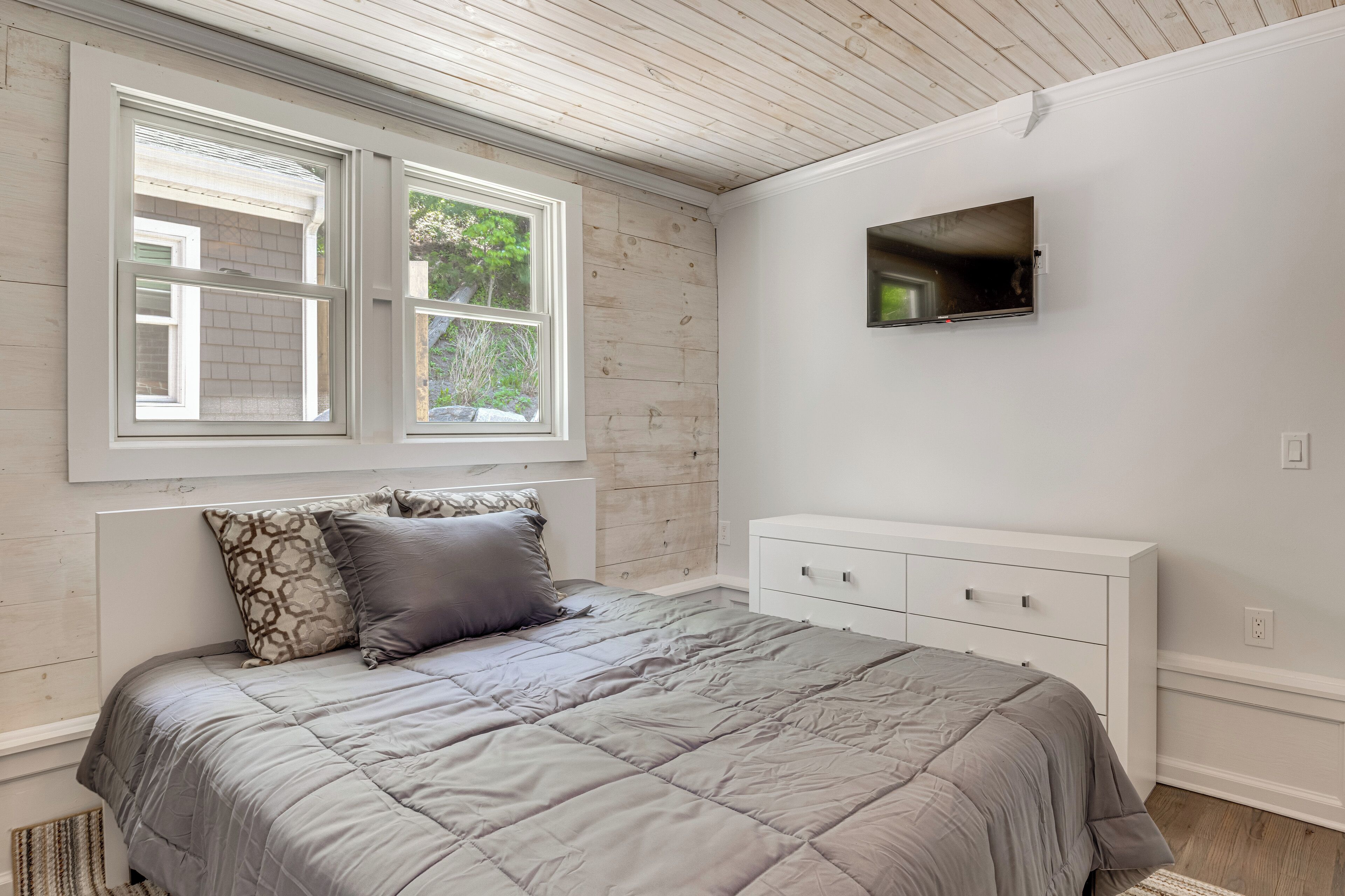 A bedroom with a bed, a dresser, a TV, and two windows.