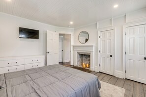 A bedroom with a bed, a fireplace, white doors, and a television on the wall. - Main St Retreat! 1895 Farmhouse in Port Jefferson (Port Jefferson)