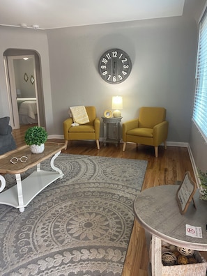 A living room with a patterned rug, two yellow armchairs, a round table with a lamp, a wall clock, and a small plant. - Hidden Gem close to I-5, 10 min. to downtown 2 bedroom w/AC in charming Salem OR (Salem)