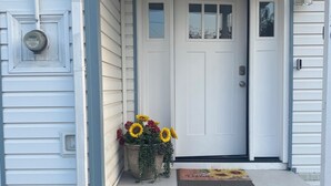 Una casa con puerta principal, un porche pequeño, un buzón y una maceta con flores.