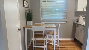 Cocina compacta con una mesa, sillas, una planta en maceta y un ventanal con persianas.