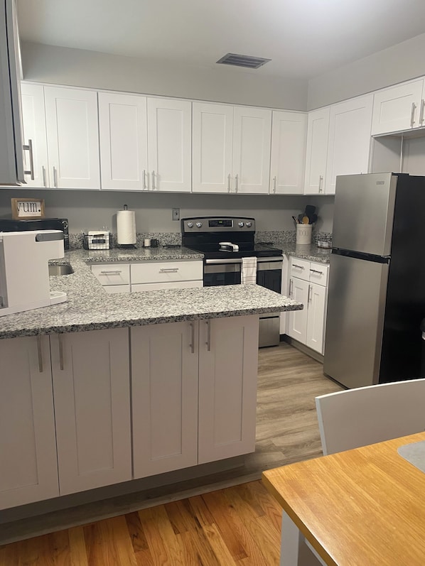 A kitchen with white cabinets, a granite countertop, a stainless steel refrigerator, and a wooden dining table. - Hidden Gem close to I-5, 10 min. to downtown 2 bedroom w/AC in charming Salem OR (Salem)