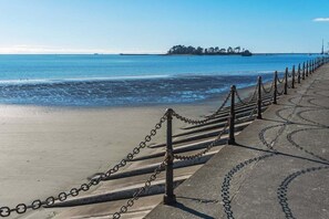 A coastal walkway with a chain barrier, leading to a beach with calm waters and a distant island. - Moana Sands - Beachside Apartment (Nelson)