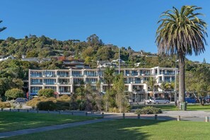 A multi-story hotel with a modern architectural design, located in a hilly area with lush greenery and a palm tree. - Moana Sands - Beachside Apartment (Nelson)